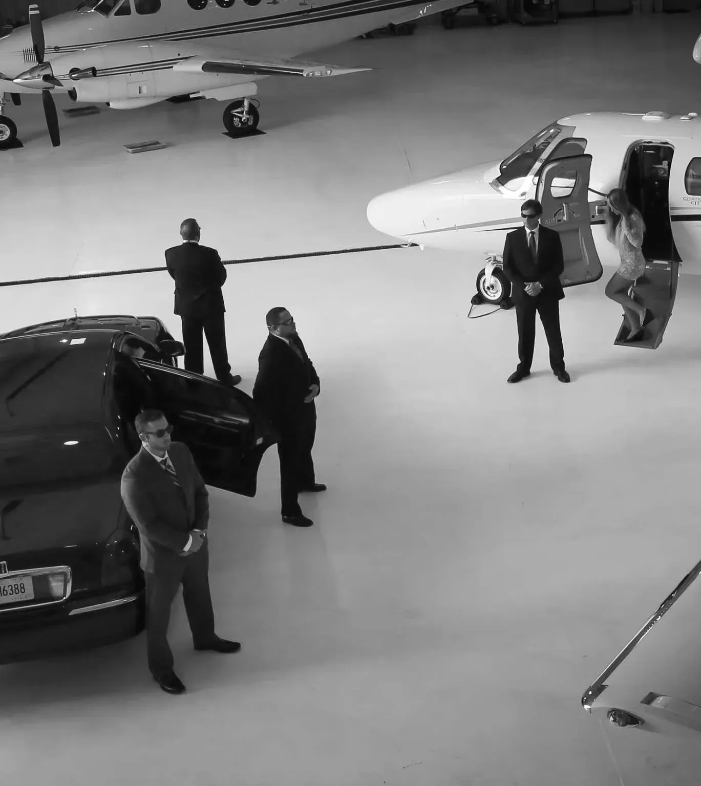 Close protection officers in suits escorting a client between a private jet and a vehicle
